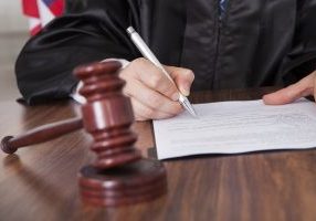 Close-up Of Male Judge Writing On Paper In Courtroom